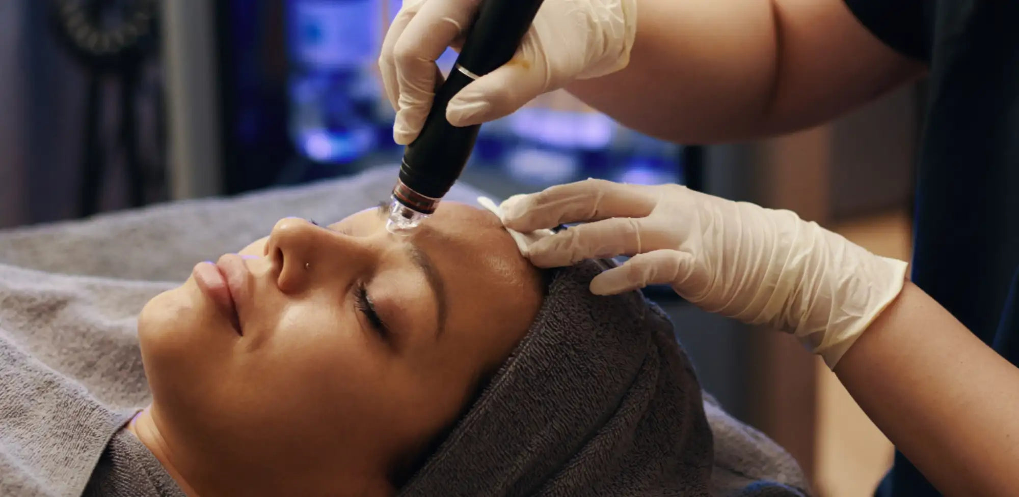 Black handheld facial device with a clear, rounded tip being used on the forehead.