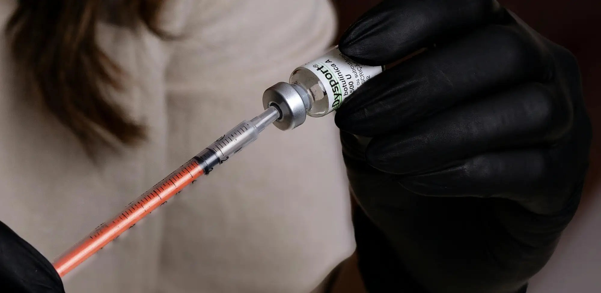 A clear glass vial with a silver cap and green labeling, containing a white liquid.