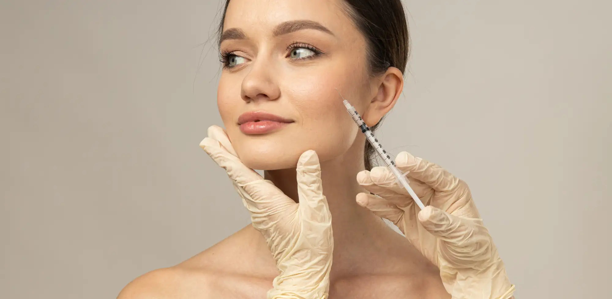 A white medical syringe with a clear barrel and black measurement markings, held by gloved hands.